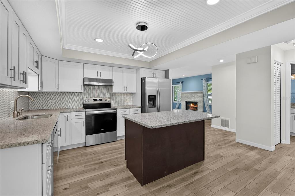 A kitchen features white cabinets, a dark island, stainless steel appliances, and wood-look flooring — 2129 LINWOOD DRIVE, SARASOTA, FL