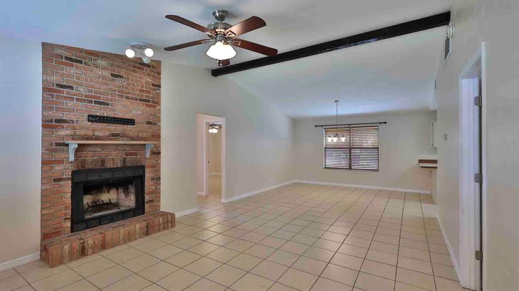 A living room features a brick fireplace, tile flooring, a ceiling fan, and vaulted ceilings — 1618 WILLOW OAK DRIVE, EDGEWATER, FL