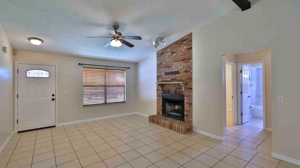 A living room features a brick fireplace, tile flooring, a ceiling fan, and an entryway — 1618 WILLOW OAK DRIVE, EDGEWATER, FL
