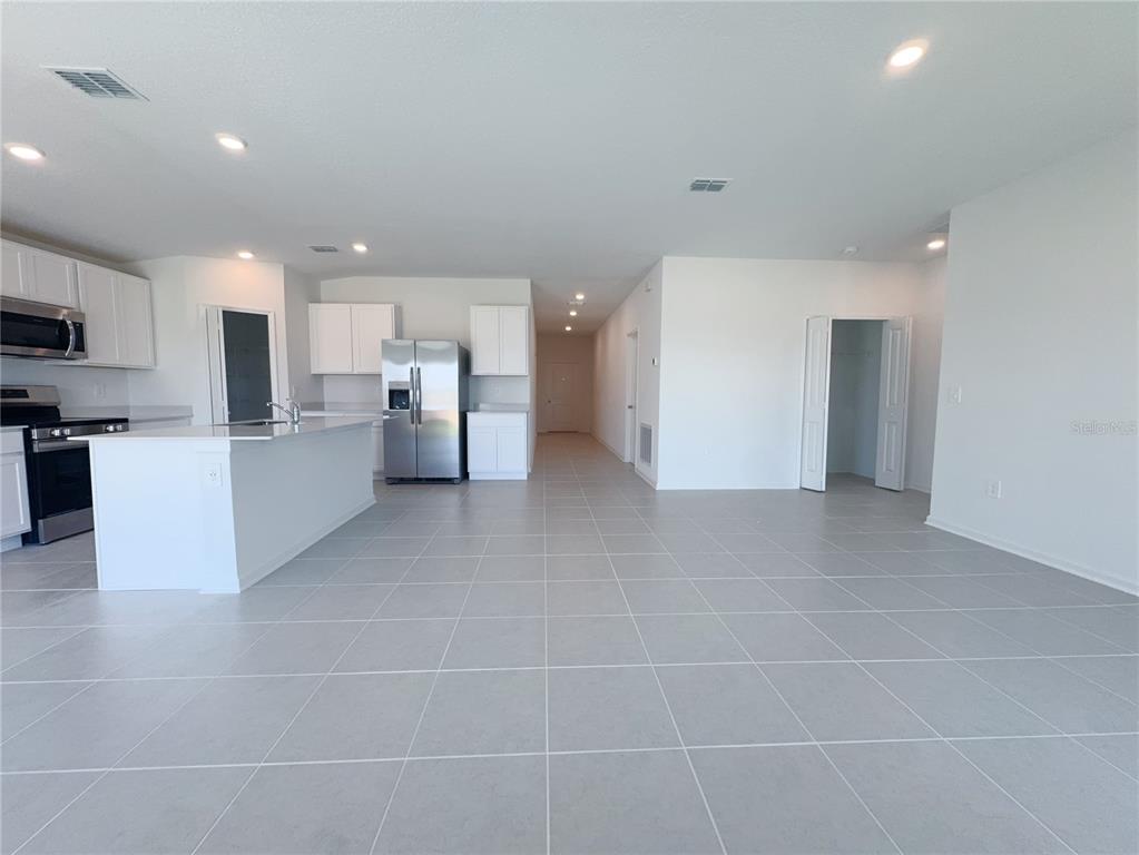 A kitchen with white cabinets and stainless steel appliances opens to a tiled living area — 2362 MCKINLEY DRIVE, LAKE WALES, FL
