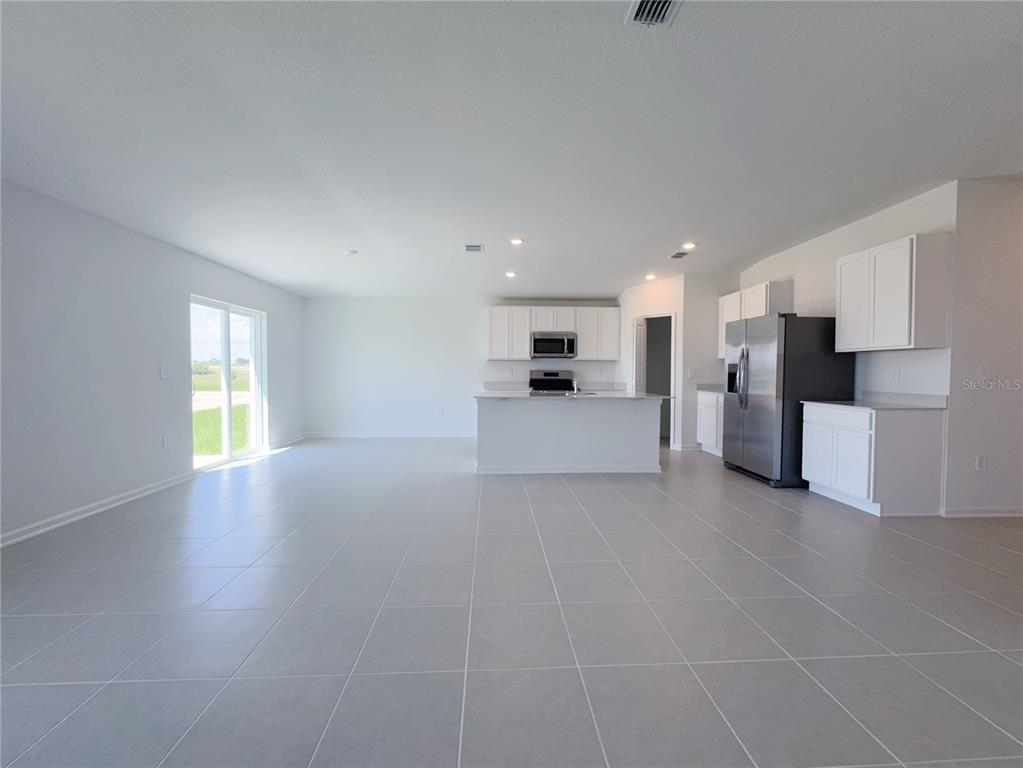A kitchen with white cabinets and stainless steel appliances opens into a large tiled room — 2362 MCKINLEY DRIVE, LAKE WALES, FL