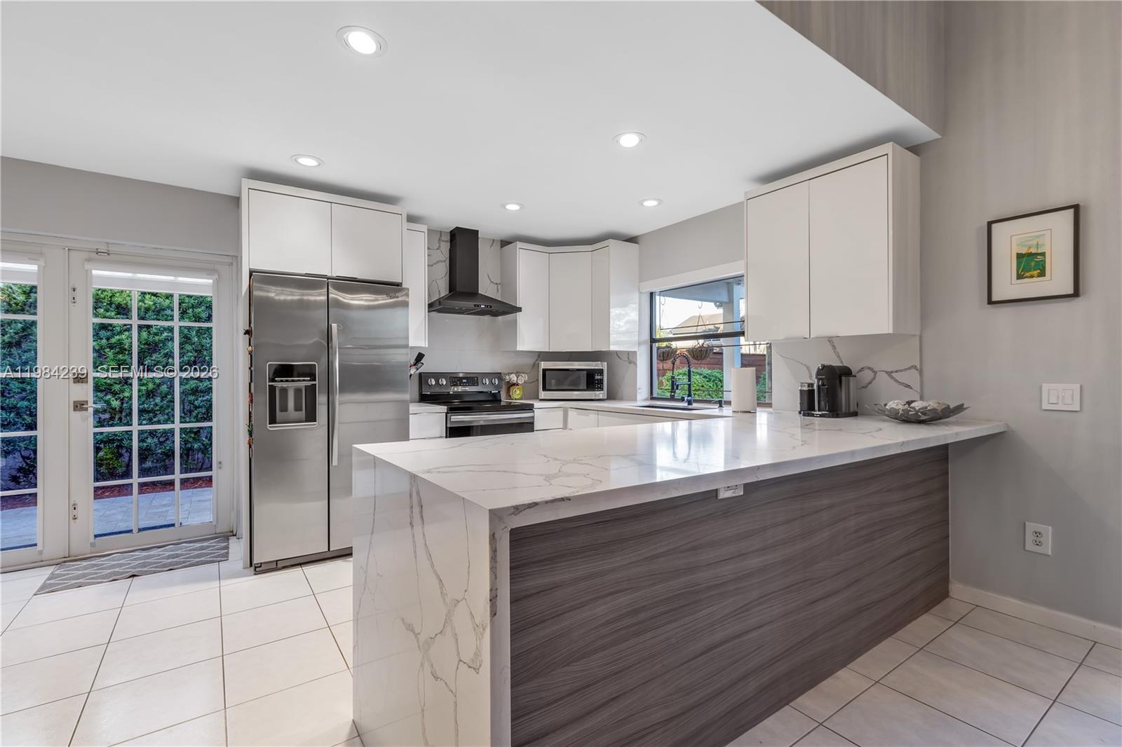 A modern kitchen features white cabinetry, marble-patterned countertops, stainless steel appliances, and a wood-paneled island — 5321 SW 153rd Pl S, Miami FL 33185, MIAMI, FL
