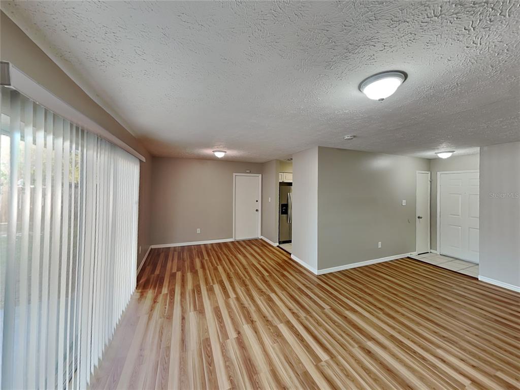 An open-concept living area features wood-look flooring, light-colored walls, and a sliding glass door — 2704 MANOR HILL DRIVE, BRANDON, FL