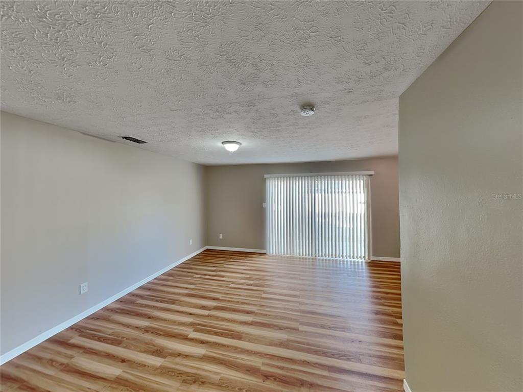 An empty living room features light wood-look flooring, beige walls, and a sliding glass door — 2704 MANOR HILL DRIVE, BRANDON, FL