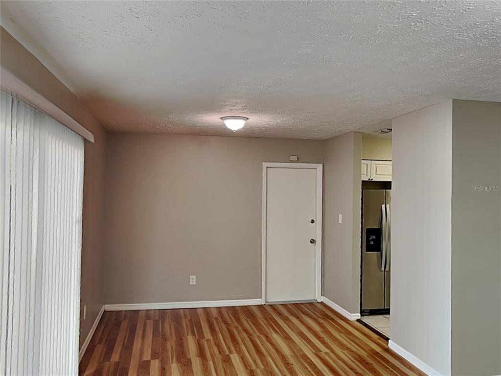 A room with wood-look flooring, a white door, and a view into a kitchen — 2704 MANOR HILL DRIVE, BRANDON, FL