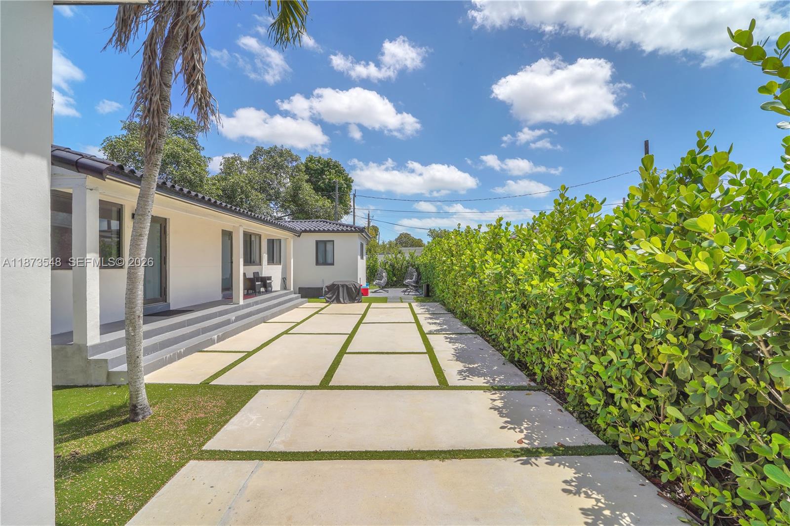A paved patio with artificial turf borders sits beside a white house and tall hedge — 621 SW 33RD AVENUE, Miami FL 33135, MIAMI, FL