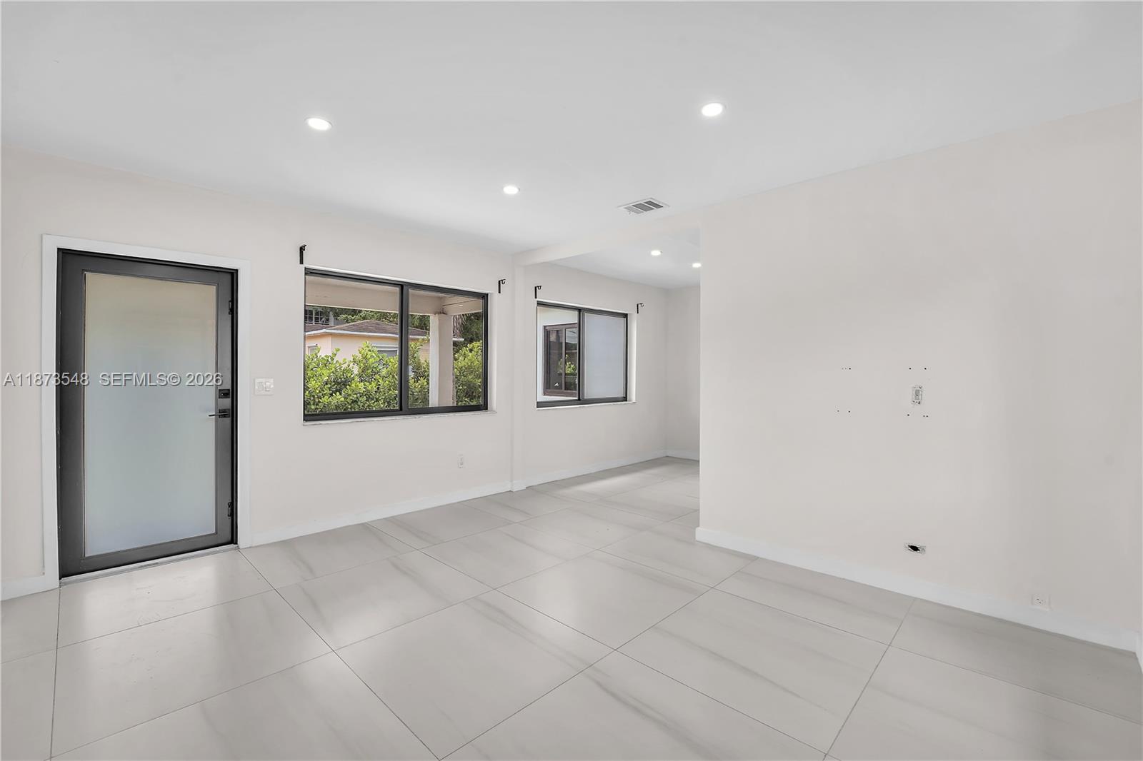 A bright, minimalist room features large light-colored floor tiles, white walls, and several windows — 621 SW 33RD AVENUE, Miami FL 33135, MIAMI, FL