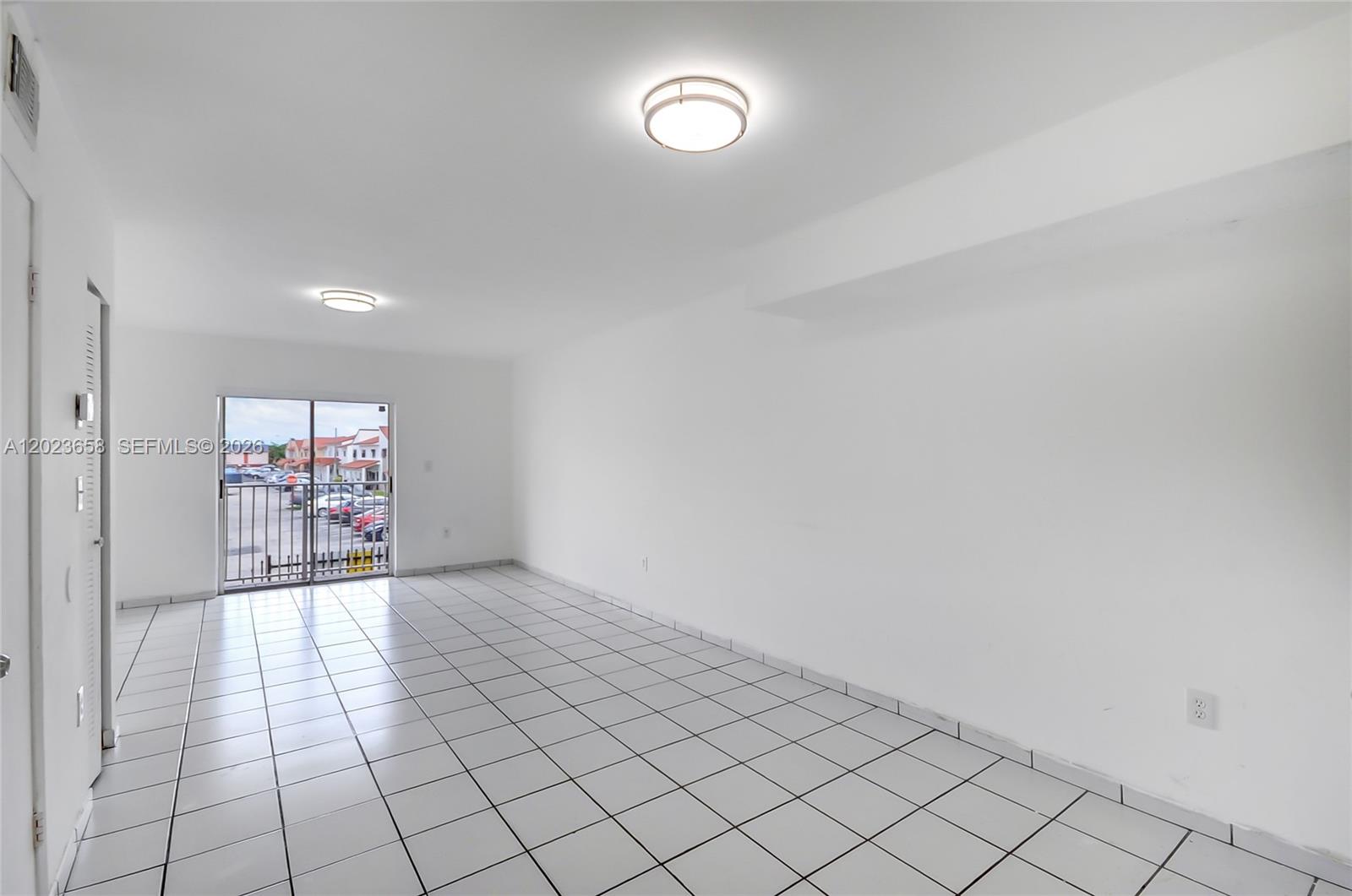 An empty room features white walls, white tiled flooring, two ceiling lights, and a sliding door — 3021 W 76th St # 203, Hialeah FL 33018, HIALEAH, FL