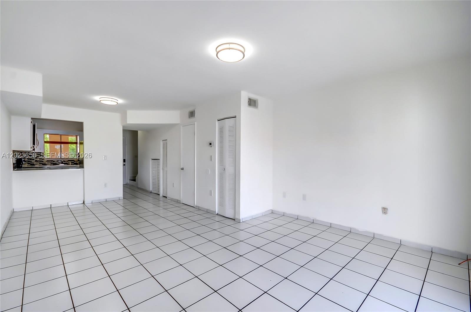 An empty room with white walls, white tiled floors, and a small kitchen visible — 3021 W 76th St # 203, Hialeah FL 33018, HIALEAH, FL