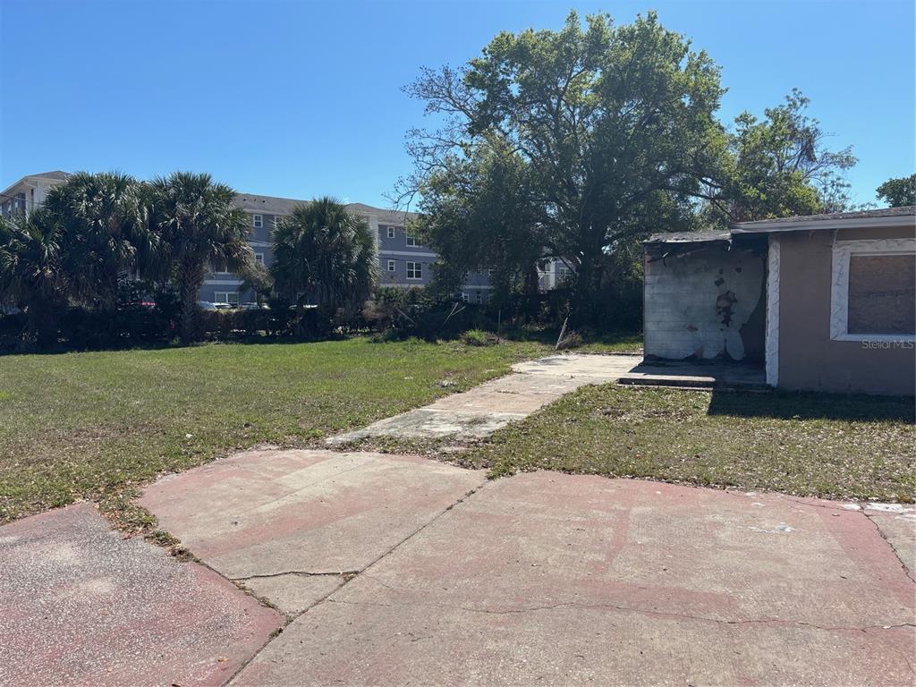 A concrete driveway leads to a damaged building exterior and a large, grassy yard — 403 MERCADO AVENUE, ORLANDO, FL