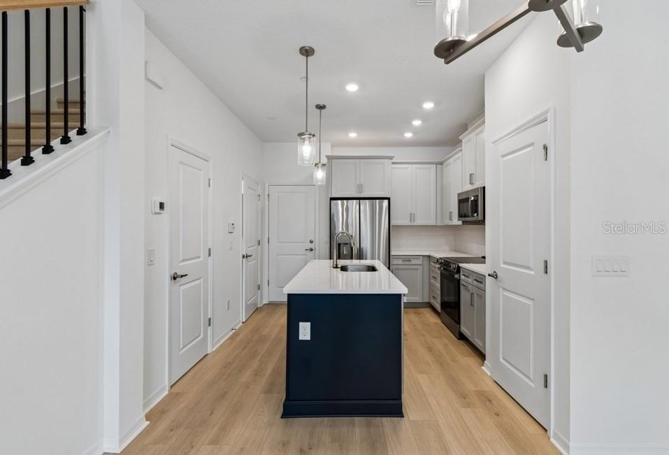 A kitchen features a dark blue island, white cabinets, stainless steel appliances, and light wood flooring — 4365 ROUSH AVENUE, ORLANDO, FL