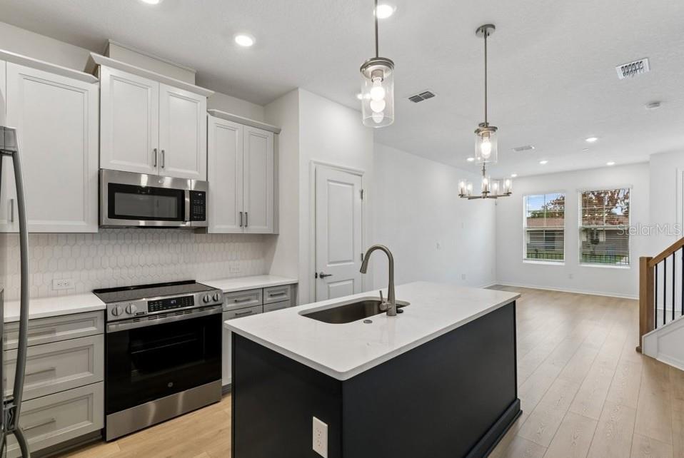 A kitchen with white cabinets, a dark island, stainless steel appliances, and light wood flooring — 4365 ROUSH AVENUE, ORLANDO, FL