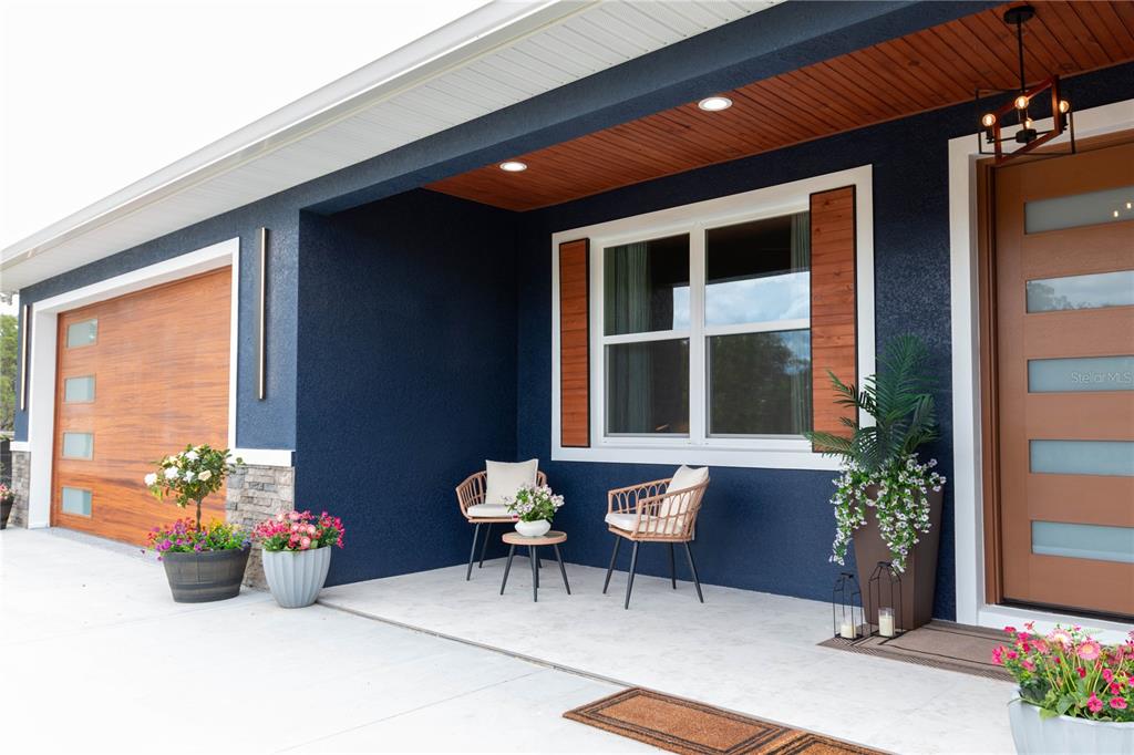 A blue-stucco front porch features two wicker chairs, a small table, and a wooden door — 6254 W PEKING COURT, DUNNELLON, FL