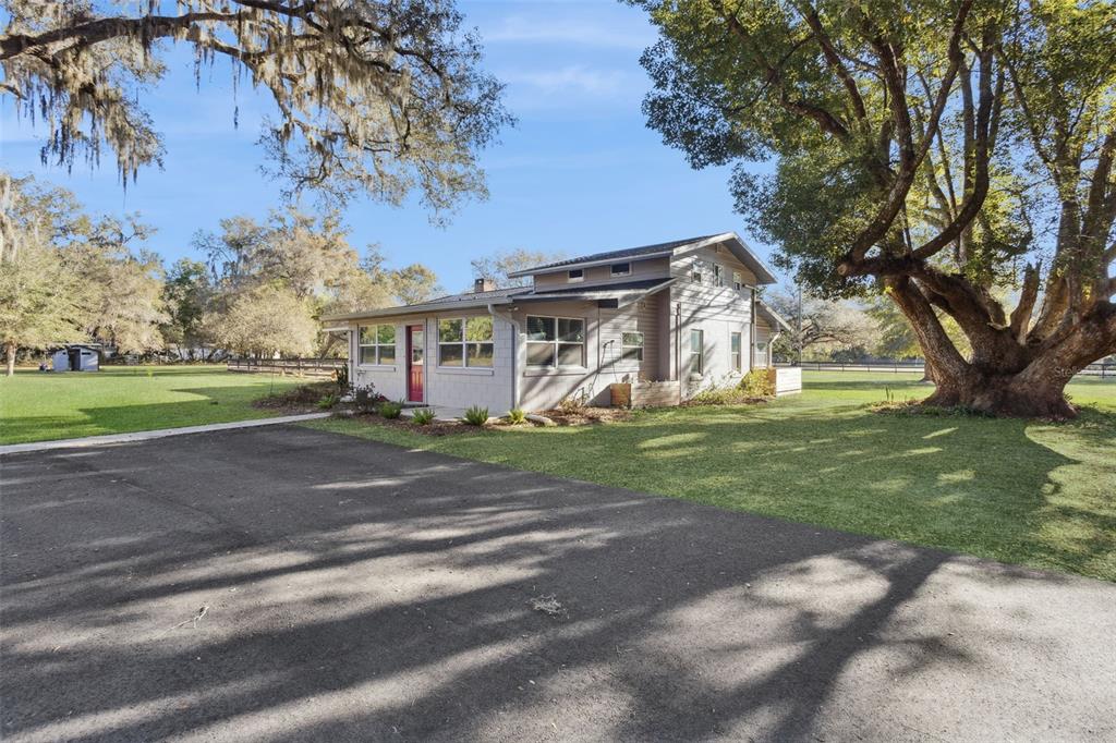 A light-colored house with a red door sits on a grassy lot with large trees — 43411 STATE ROAD 19, ALTOONA, FL