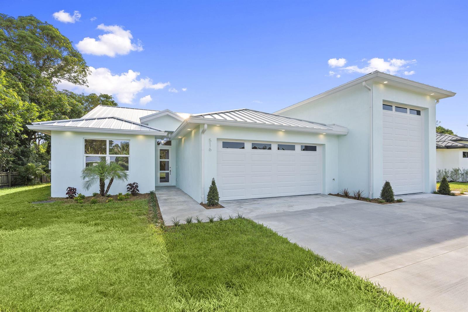 A light blue single-story house features a metal roof, two garage doors, and a walkway — 516 SE Alamanda Way, Stuart FL 34996, STUART, FL