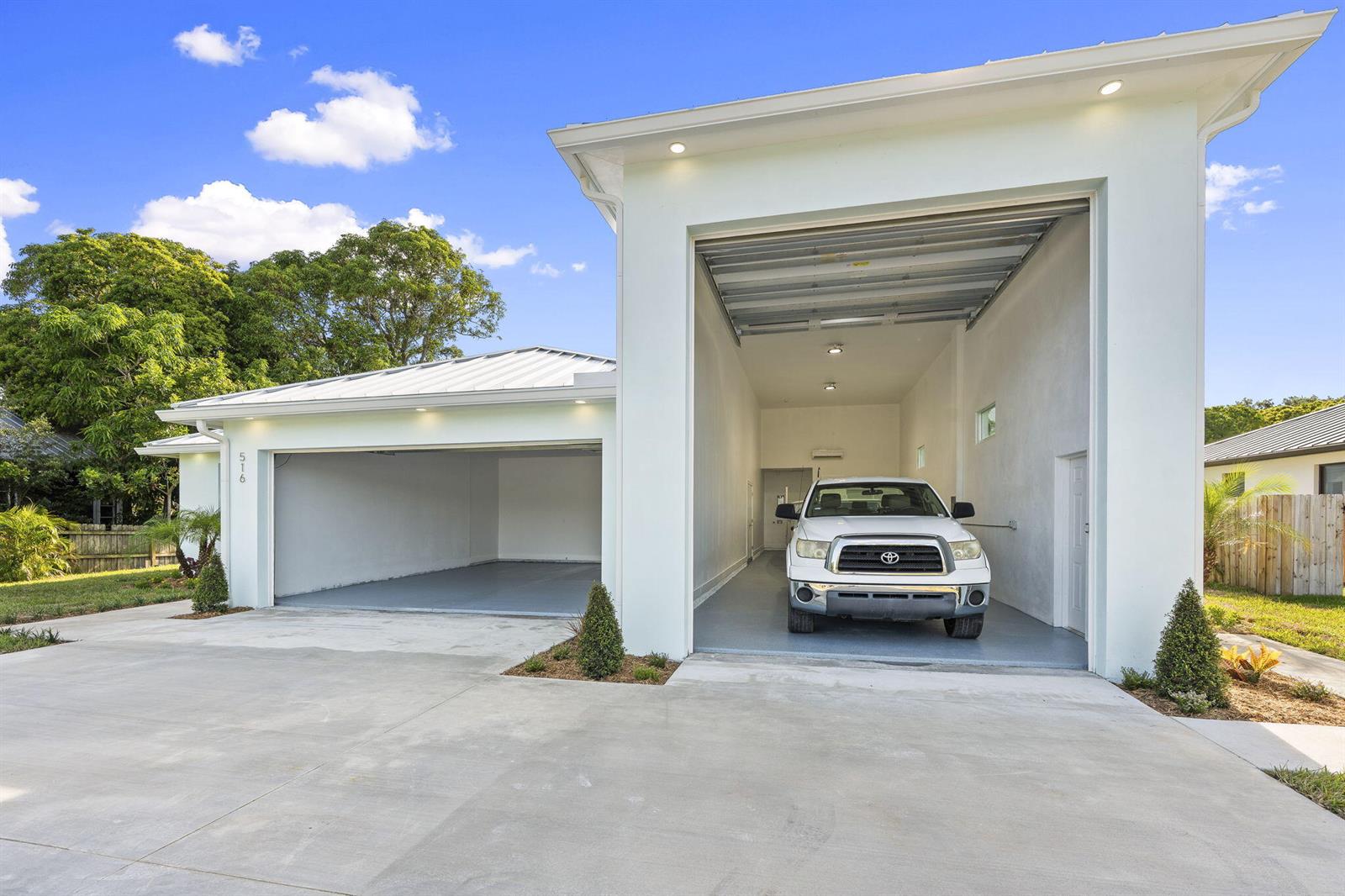 A white house features a standard garage and an adjacent high-ceilinged bay housing a truck — 516 SE Alamanda Way, Stuart FL 34996, STUART, FL