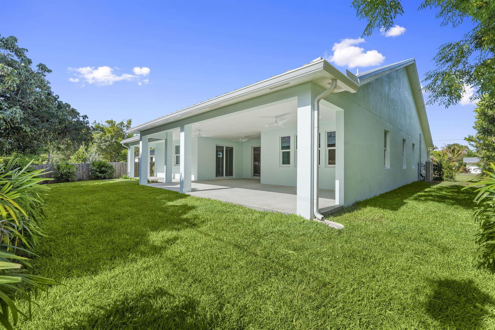 A light green house features a large covered concrete patio overlooking a grassy backyard — 516 SE Alamanda Way, Stuart FL 34996, STUART, FL