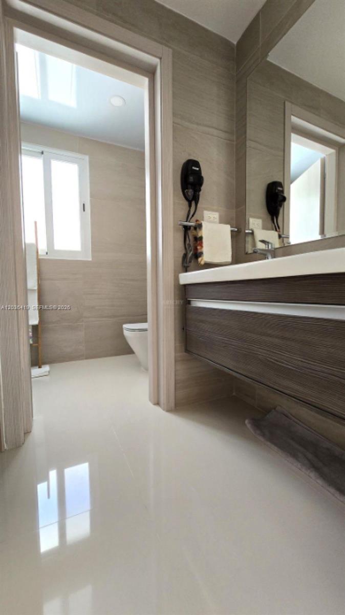 A modern bathroom features a floating wood vanity, a large mirror, and a separate toilet area — 0 Cocotal # 0, FL, FL