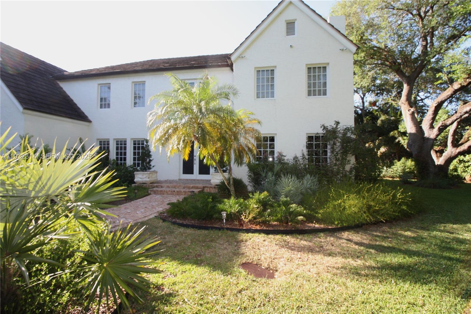 A two-story white house features a brick walkway, a palm tree, and mature landscaping — 6750 Granada Blvd, Coral Gables FL 33146, CORAL GABLES, FL