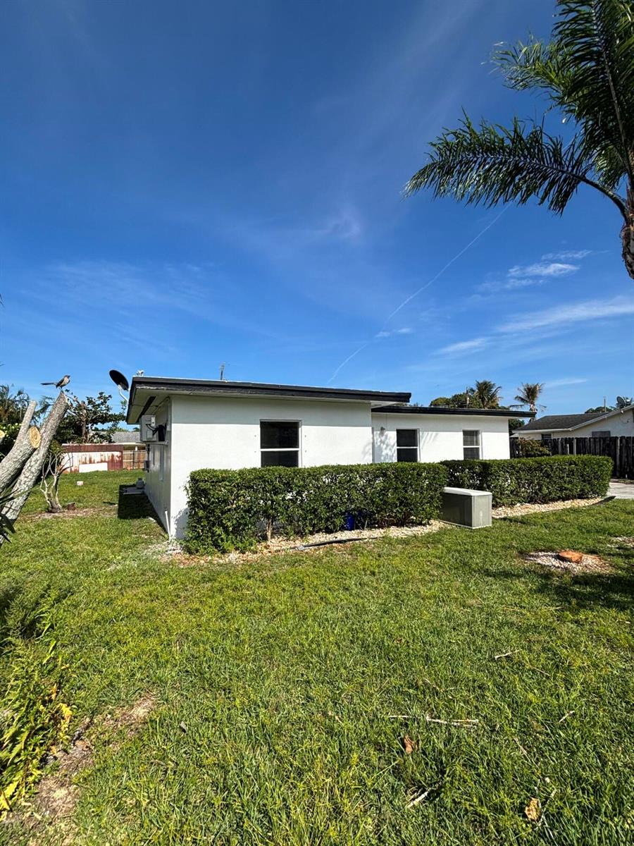 The exterior of a white, flat-roofed house features a manicured hedge and a grassy yard — 328 Urquhart Street, FL 33461, FL