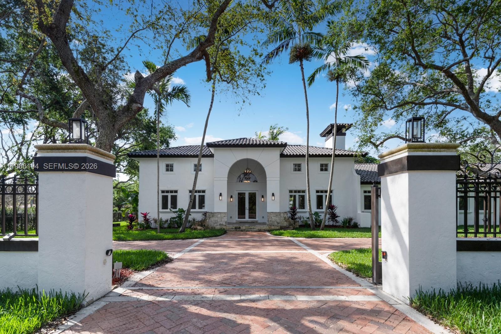 A white two-story house with a tiled roof sits behind a brick driveway and gate — 6200 SW 130th Ter, Pinecrest FL 33156, PINECREST, FL