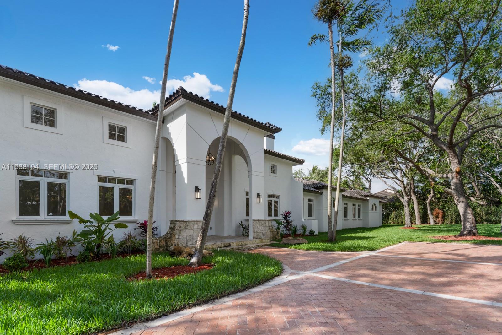 A white two-story house with a tiled roof and arched entryway sits beside a driveway — 6200 SW 130th Ter, Pinecrest FL 33156, PINECREST, FL