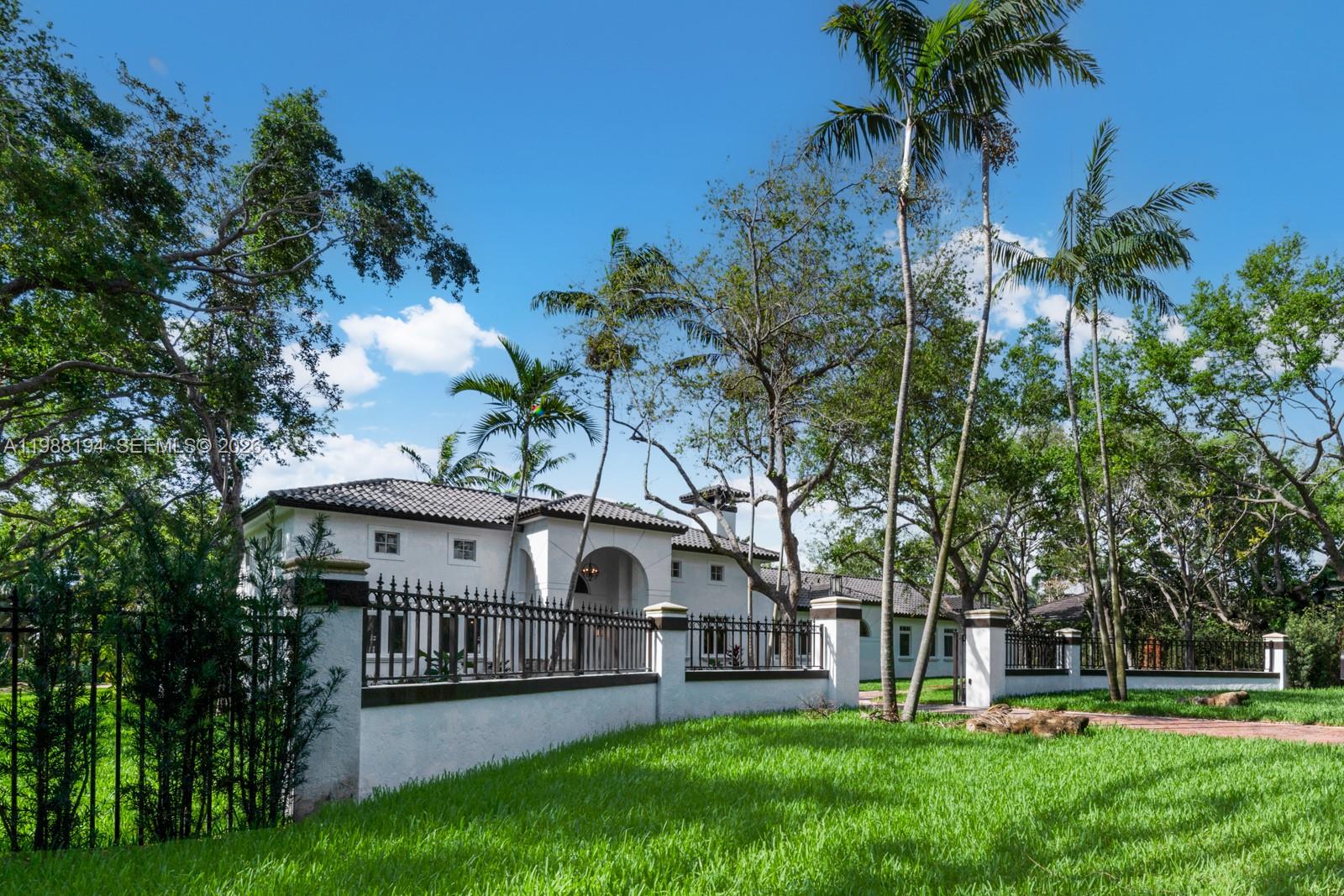 A white two-story house with a tile roof sits behind a black metal fence — 6200 SW 130th Ter, Pinecrest FL 33156, PINECREST, FL