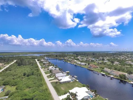 An aerial view shows a canal lined with houses leading toward a distant body of water — 10441 VAN WYCK TERRACE, PORT CHARLOTTE, FL