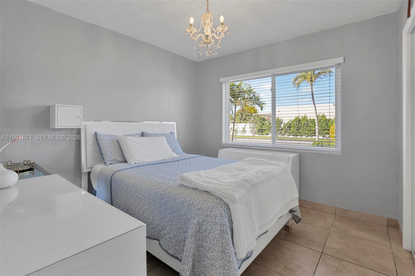 A bedroom features a bed with blue bedding, a chandelier, and a window with blinds — 1901 SW 90th Ave, Miami FL 33165, MIAMI, FL