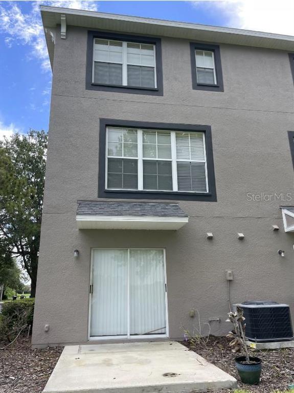 The exterior of a three-story gray stucco townhouse features a sliding glass door and windows — 2401 LEXINGTON OAK DRIVE, BRANDON, FL