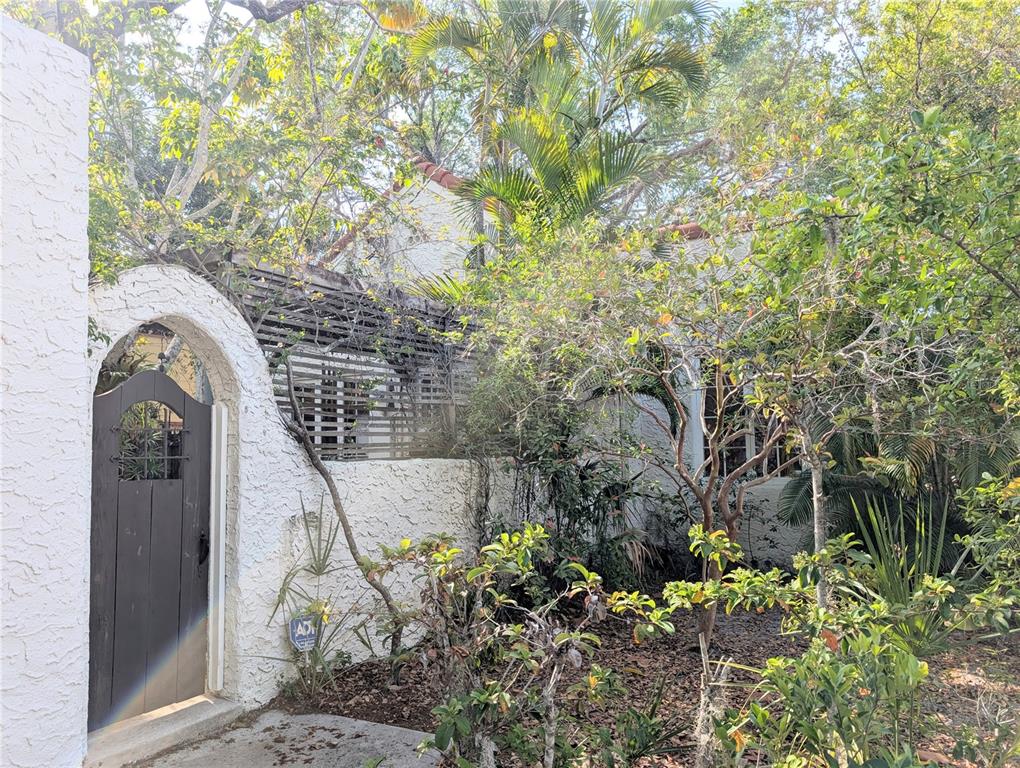 An arched wooden gate leads to a white stucco home with a wooden trellis — 1701 SIESTA DRIVE, SARASOTA, FL