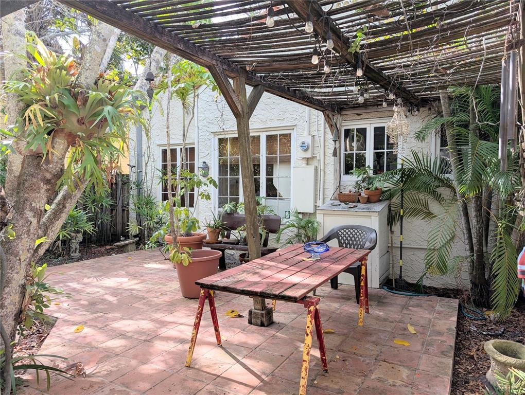 A patio with a wooden pergola, a red table, and potted plants outside a house — 1701 SIESTA DRIVE, SARASOTA, FL