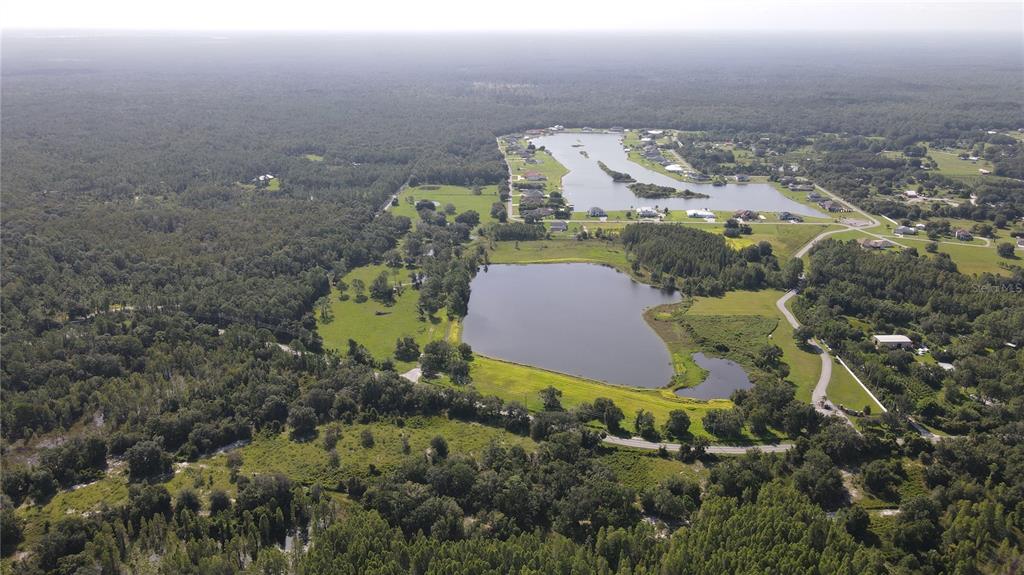 An aerial view shows two lakes surrounded by green fields, trees, and residential houses — 10460 EHREN CUTOFF, LAND O LAKES, FL