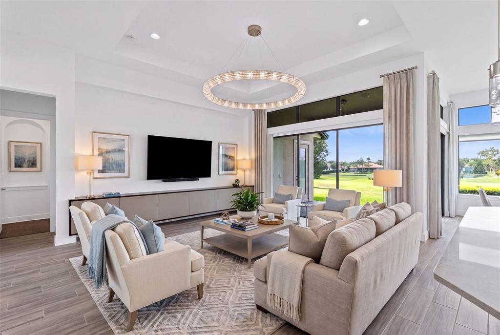 A bright living room features a large circular chandelier, neutral furniture, and floor-to-ceiling windows — 25858 CROSSINGS BLUFF LANE, SORRENTO, FL
