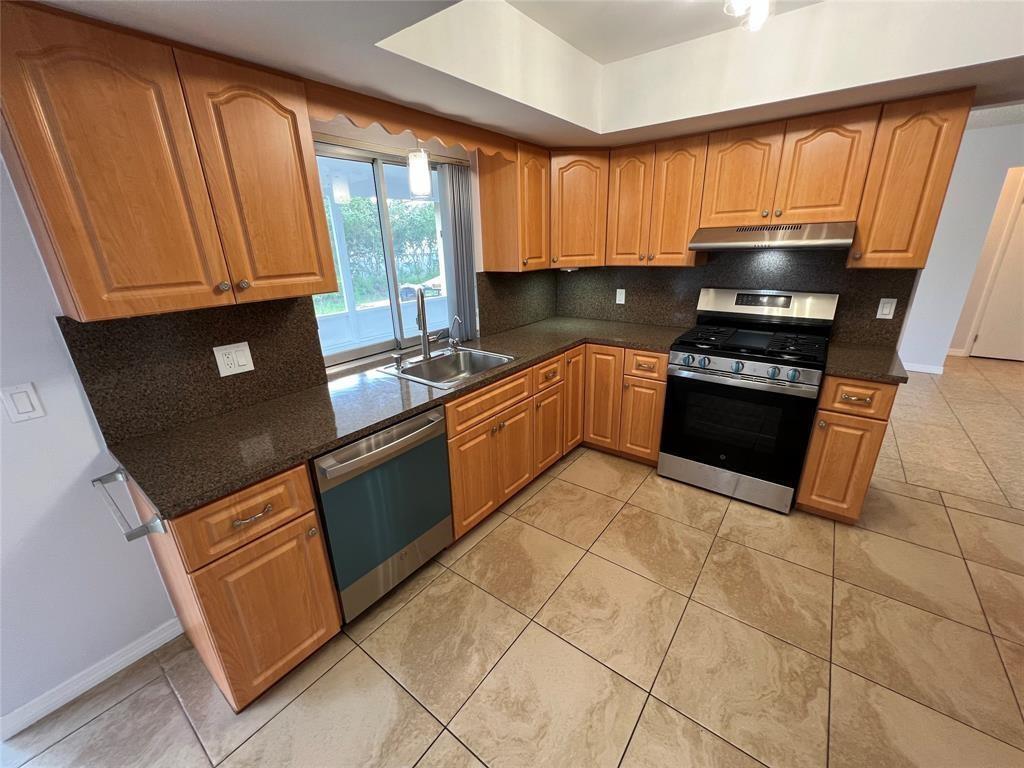 A kitchen features wood cabinets, dark granite countertops, stainless steel appliances, and beige tile flooring — 2650 NW 94th Way, Sunrise FL 33322, SUNRISE, FL