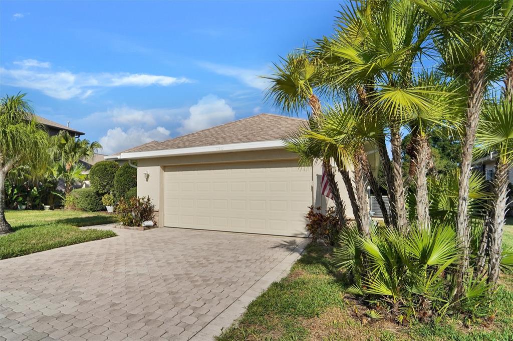 A beige house with a two-car garage and a paved driveway sits behind palm trees — 740 SALT LAKE DRIVE, TARPON SPRINGS, FL