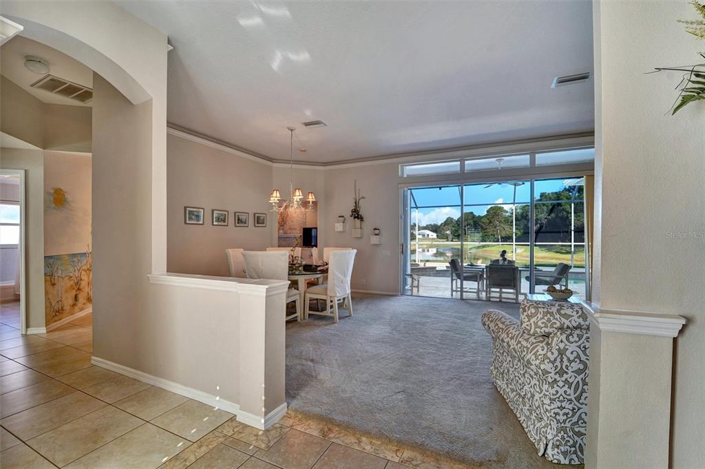 A dining area and living space feature carpeted floors, a chandelier, and sliding glass doors — 740 SALT LAKE DRIVE, TARPON SPRINGS, FL