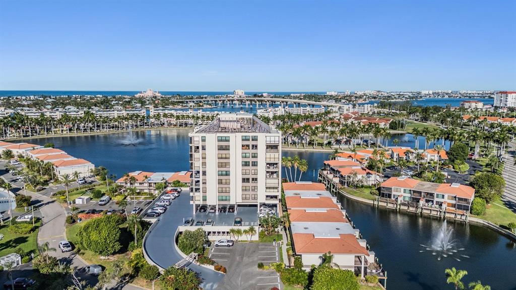 An aerial view shows a multi-story apartment building surrounded by water, palm trees, and parking — 6294 BAHIA DEL MAR CIRCLE UNIT 107, ST PETERSBURG, FL