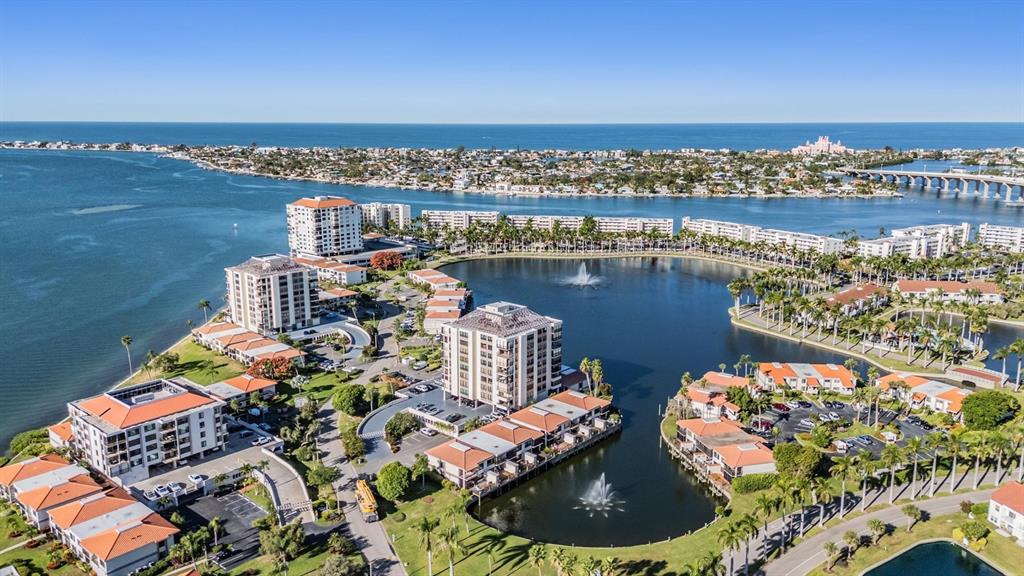 An aerial view shows waterfront apartment buildings surrounding a lake with fountains and palm trees — 6294 BAHIA DEL MAR CIRCLE UNIT 107, ST PETERSBURG, FL