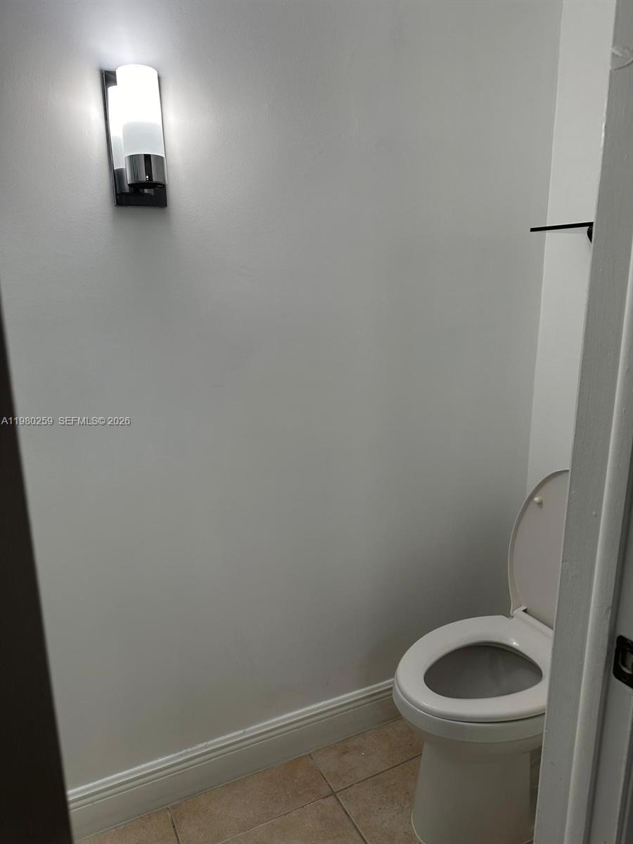 A small bathroom features a white toilet, light-colored tile flooring, and a wall-mounted light fixture — 8500 SW 109th Ave # 202, Miami FL 33173, MIAMI, FL