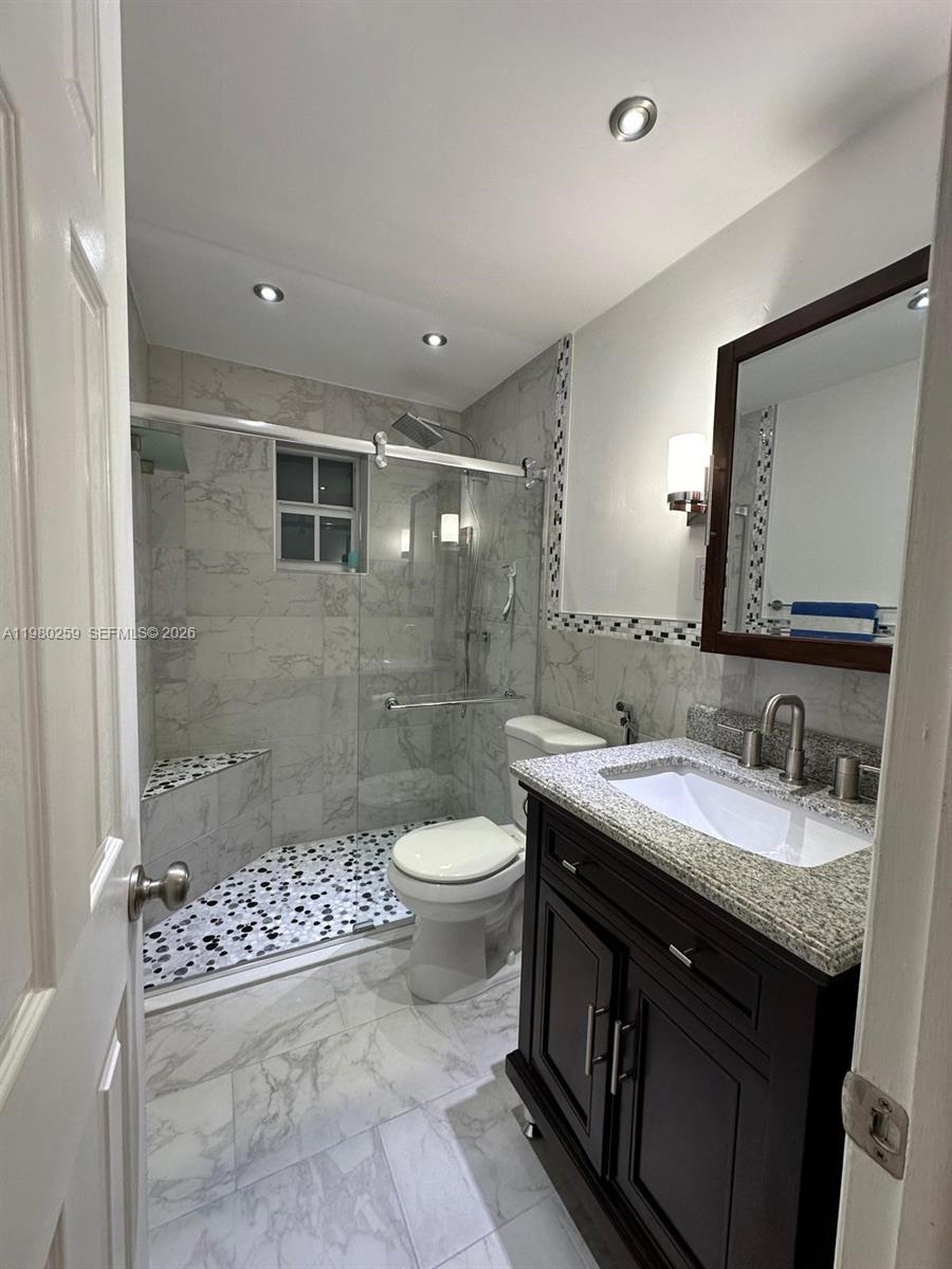 A bathroom features a glass-enclosed shower with pebble flooring, a vanity, and marble-style tiles — 8500 SW 109th Ave # 202, Miami FL 33173, MIAMI, FL