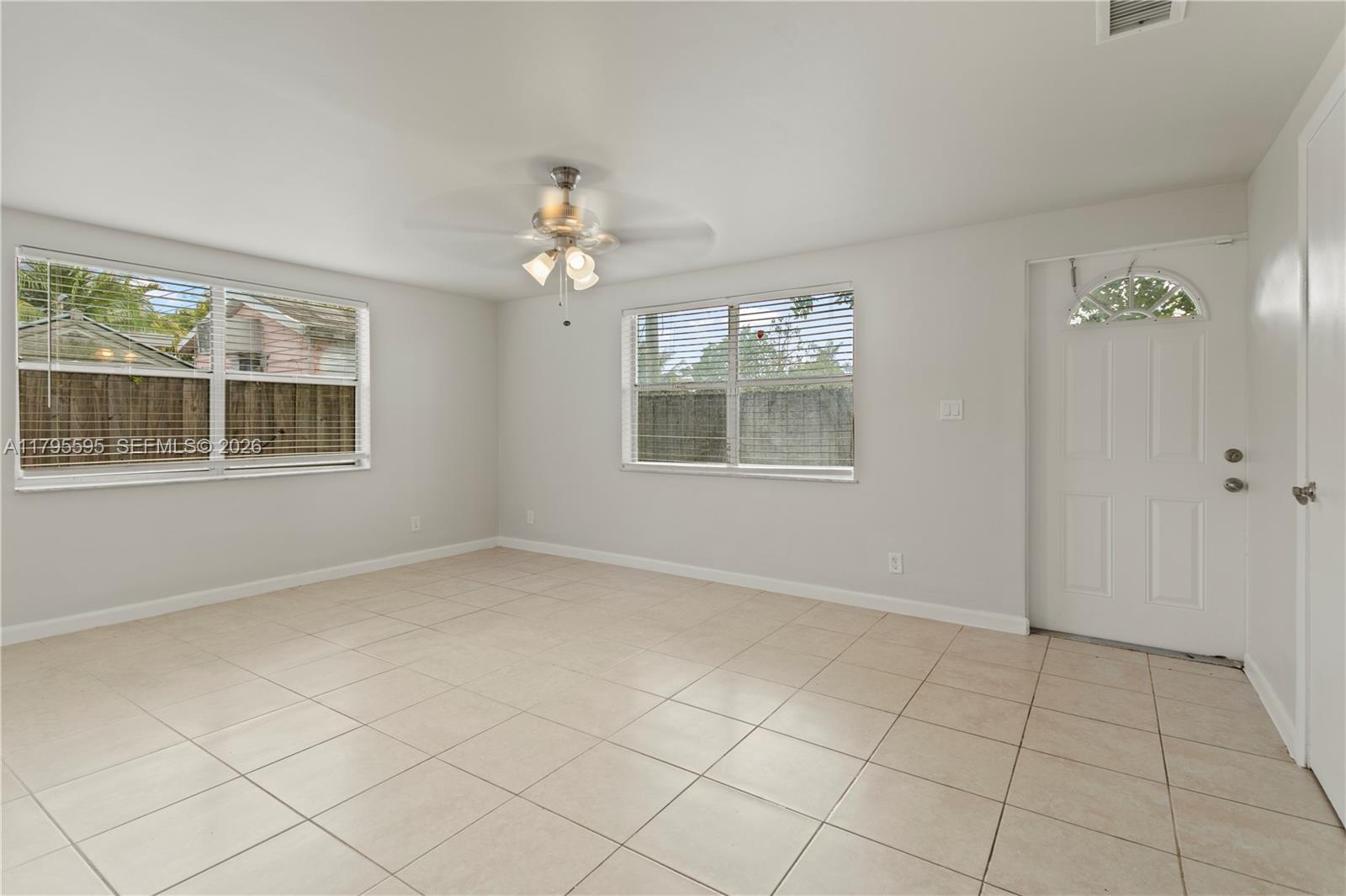 An empty room features white walls, light-colored tile flooring, two windows, and a ceiling fan — 3121 NE 13th Ave, Pompano Beach FL 33064, POMPANO BEACH, FL