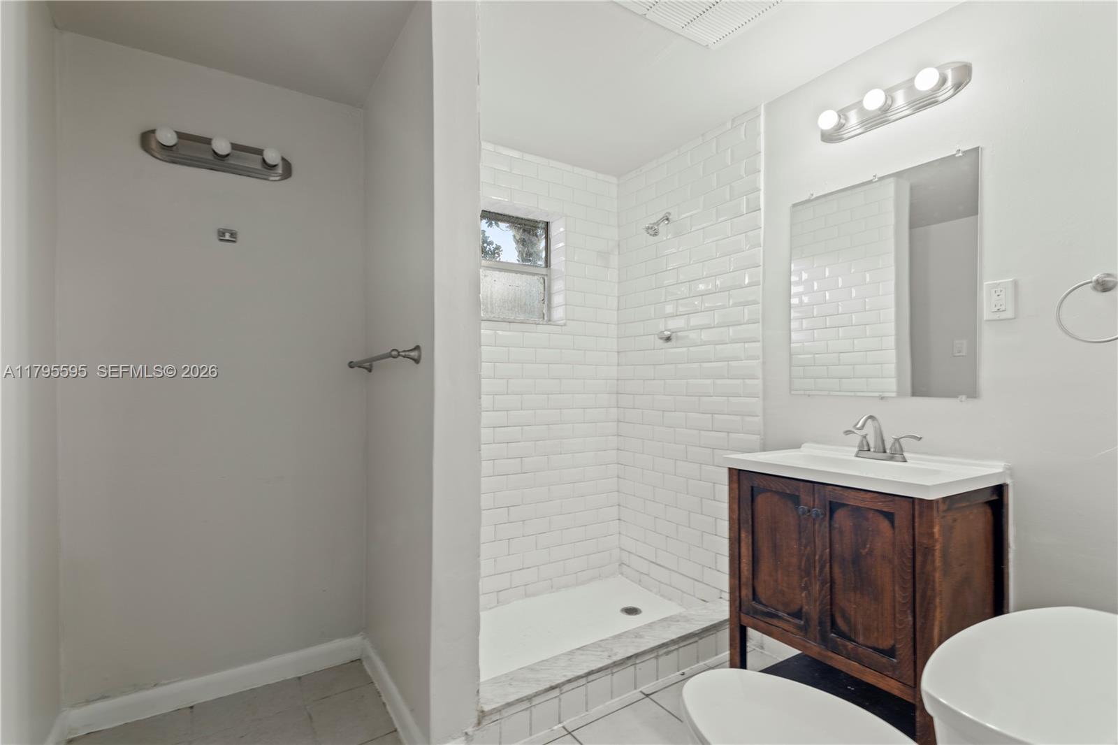 A bathroom features a walk-in shower with white subway tiles, a wood vanity, and lighting — 3121 NE 13th Ave, Pompano Beach FL 33064, POMPANO BEACH, FL