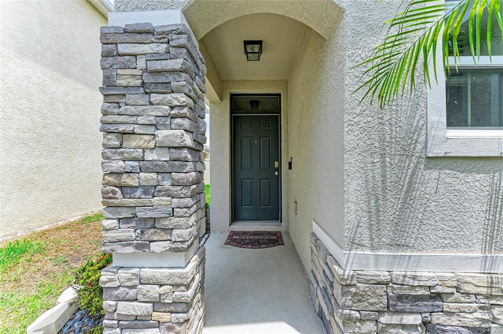A covered entryway features a dark front door, stone pillar, and stucco exterior walls — 5908 BRIAR ROSE WAY, SARASOTA, FL