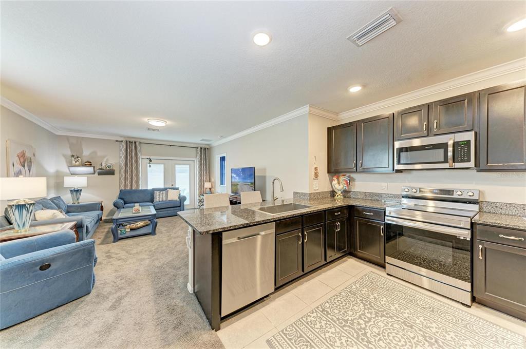 An open-concept kitchen with dark cabinets and granite countertops overlooks a carpeted living area — 5908 BRIAR ROSE WAY, SARASOTA, FL