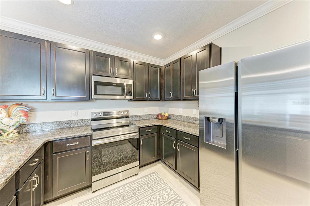 A kitchen features dark wood cabinets, granite countertops, and stainless steel appliances — 5908 BRIAR ROSE WAY, SARASOTA, FL