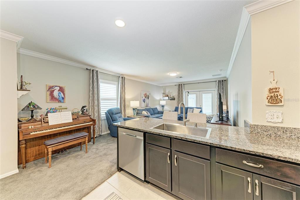 A kitchen island with granite countertops overlooks a living area featuring a piano and sofa — 5908 BRIAR ROSE WAY, SARASOTA, FL