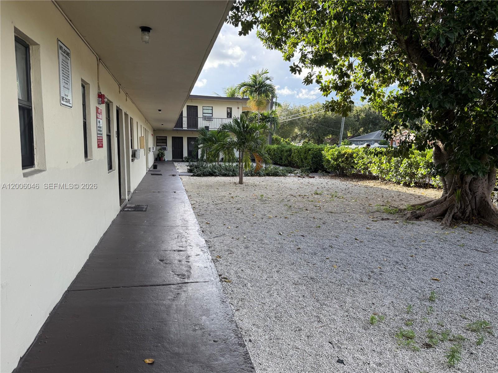 A concrete walkway runs alongside an apartment building exterior next to a gravel courtyard — 3330 NW 48th Ter # 206, Miami FL 33142, MIAMI, FL