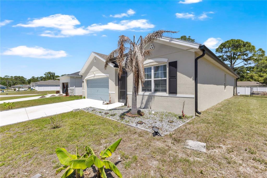 A single-story house with a light-colored stucco exterior, a two-car garage, and a palm tree — 941 CENTURY AVENUE SE, PALM BAY, FL
