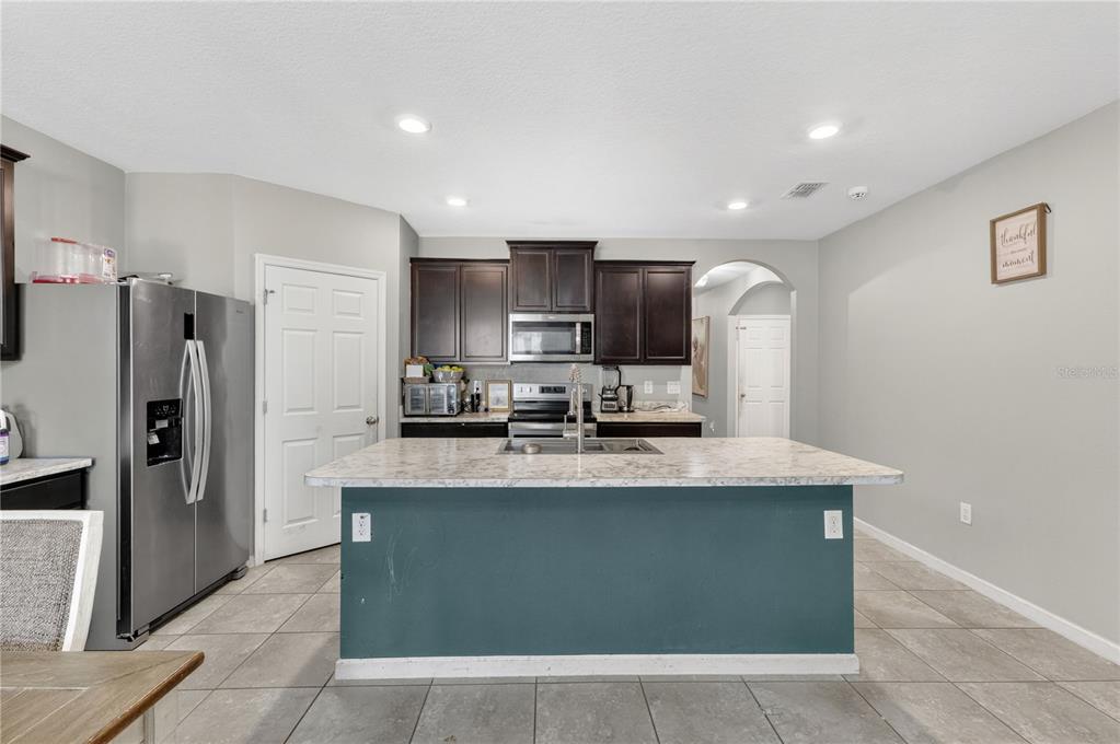A kitchen features dark wood cabinets, a teal island with a stone countertop, and tile flooring — 941 CENTURY AVENUE SE, PALM BAY, FL